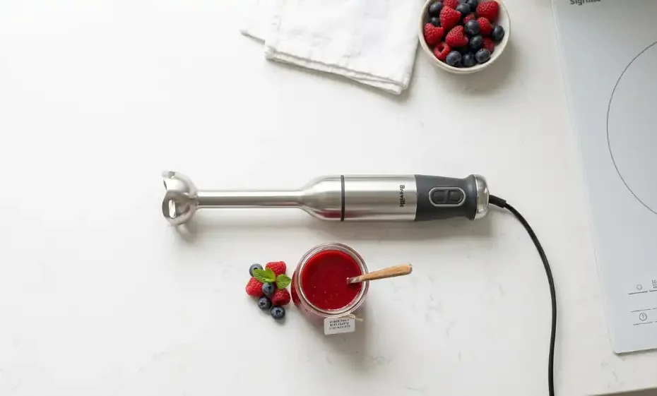 licuadora de mano moderna junto a un coulis de frutas