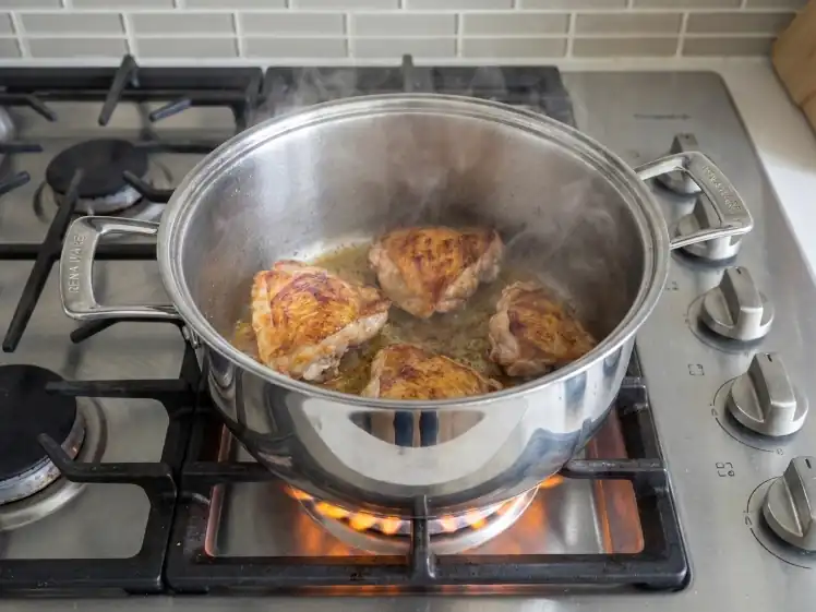 Receta de seco de pollo peruano: presas de pollo sellándose en olla de acero inoxidable